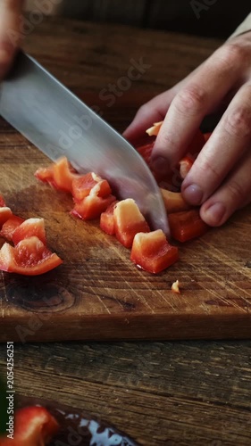 Vertical video. Cooking summer vegetables. Chopping fresh red bell pepper on cutting board