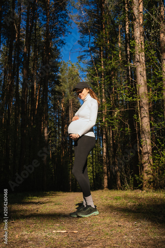 Foto Pregnant woman standing in a lush forest or park, gently holding her baby bump,