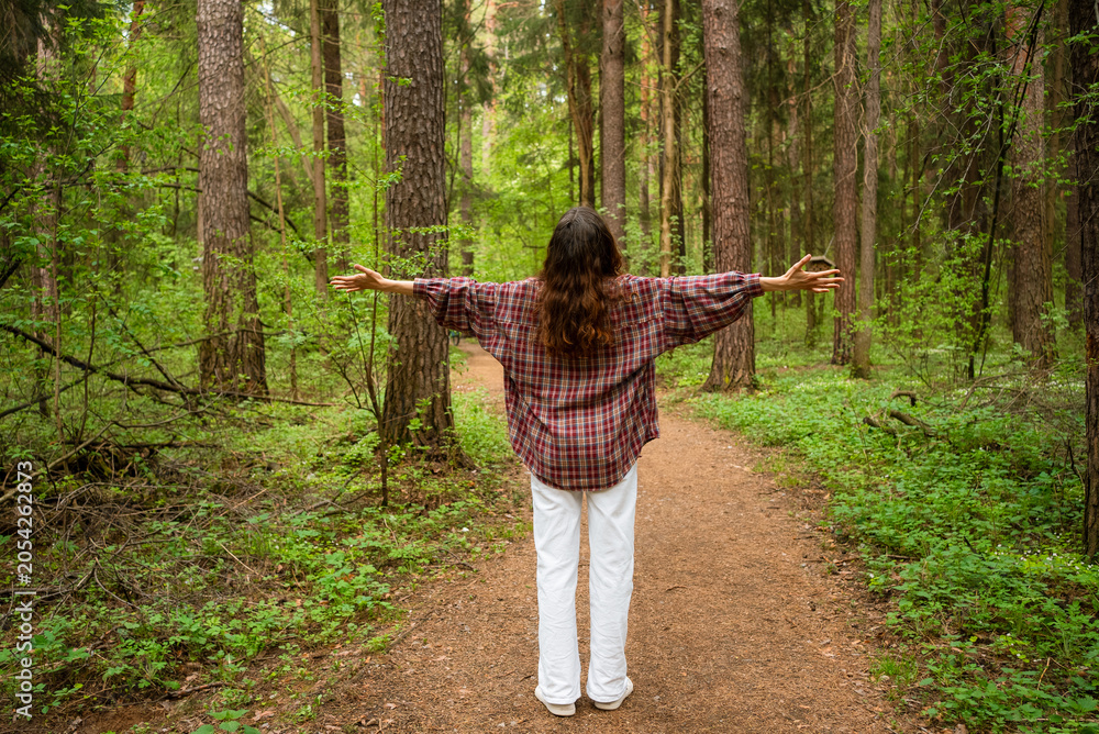 Obraz premium Pregnant woman relaxing in a forest, standing on a dirt path with arms extended, embodying freedom and connection to the environment, enjoying a healthy pregnancy outdoors