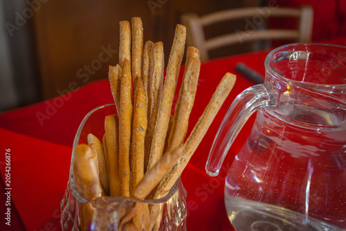 Grissini breadsticks and a water pitcher resting on a red tablecloth