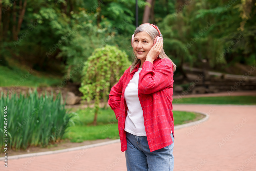 Fototapeta premium Beautiful senior woman with headphones walking in spring park