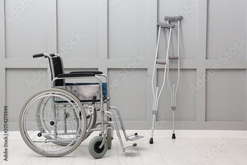 Fotografía Modern wheelchair and metal axillary crutches near grey wall indoors