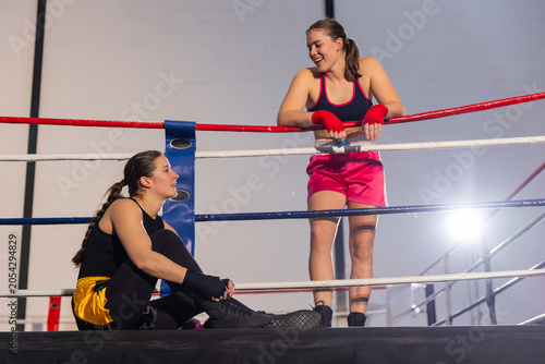 Tableau sur toile Two female boxers leaning on ropes, sitting in boxing ring wearing pink shorts a