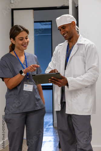 Medical coworkers reviewing tablet chart in hospital hall, wearing gray scrubs and ID badges