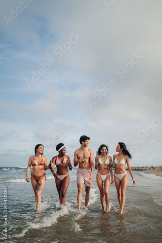 Foto Diverse friends walking on beach, enjoying summer vacation with drinks, celebrat