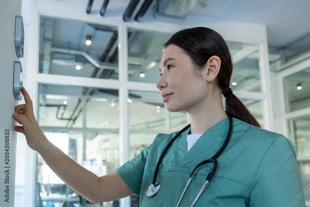 Fototapeta premium Dark-haired female doctor in lab coat setting the temperature range in a room