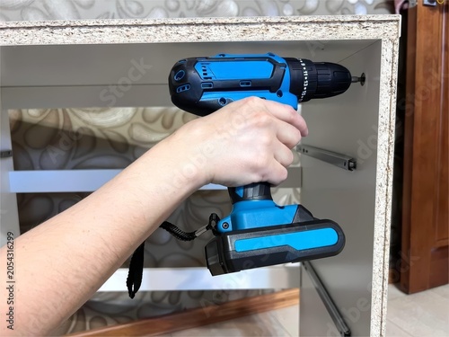 Bild auf Leinwand Hand using blue cordless drill to assemble white furniture
