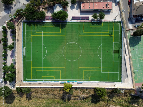 Aerial top view of a green synthetic turf soccer field featuring white lines and yellow markers for multiple sports configurations located in a modern urban sports complex park setting