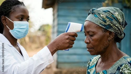 African female volunteer checking senior woman forehead temperature with infrared thermal scanner during community ebola virus epidemic prevention campaign