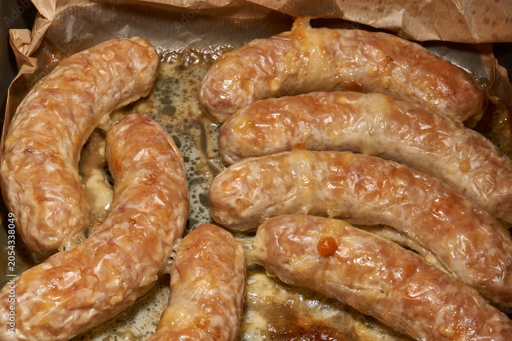 Fototapeta premium Hot homemade sausages with a juicy texture and golden surface on a parchment-lined baking tray. Golden Brown Pork Sausages Fresh from the Oven. Baked Homemade Sausages Close Up.