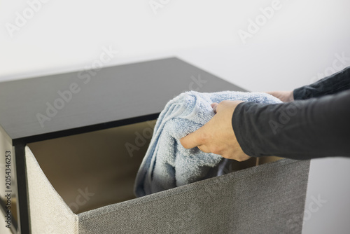 Woman putting a folded blue towel into a modern fabric storage dresser drawer.
