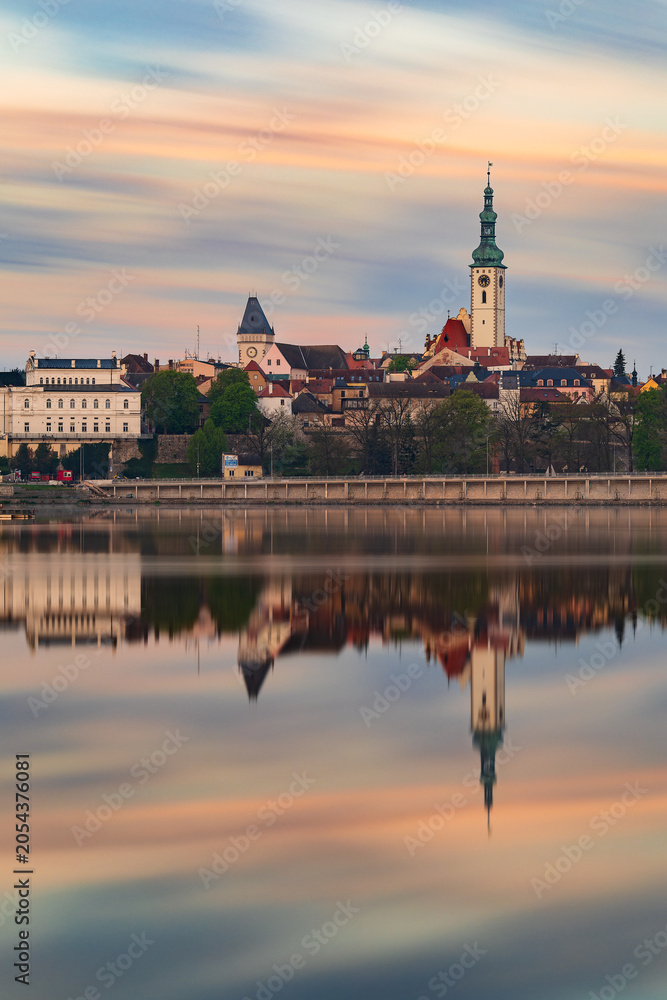 Fototapeta premium Historic center of Tabor with the Church of the Transfiguration reflected in Jordan Reservoir during colorful sunrise. Long exposure cityscape in South Bohemia, Czech Republic.
