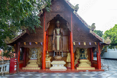 Foto A large wooden structure with intricate carvings houses several Buddha statues, including a prominent standing figure, at Wat Phra That Doi Suthep in Chiang Mai, Thailand