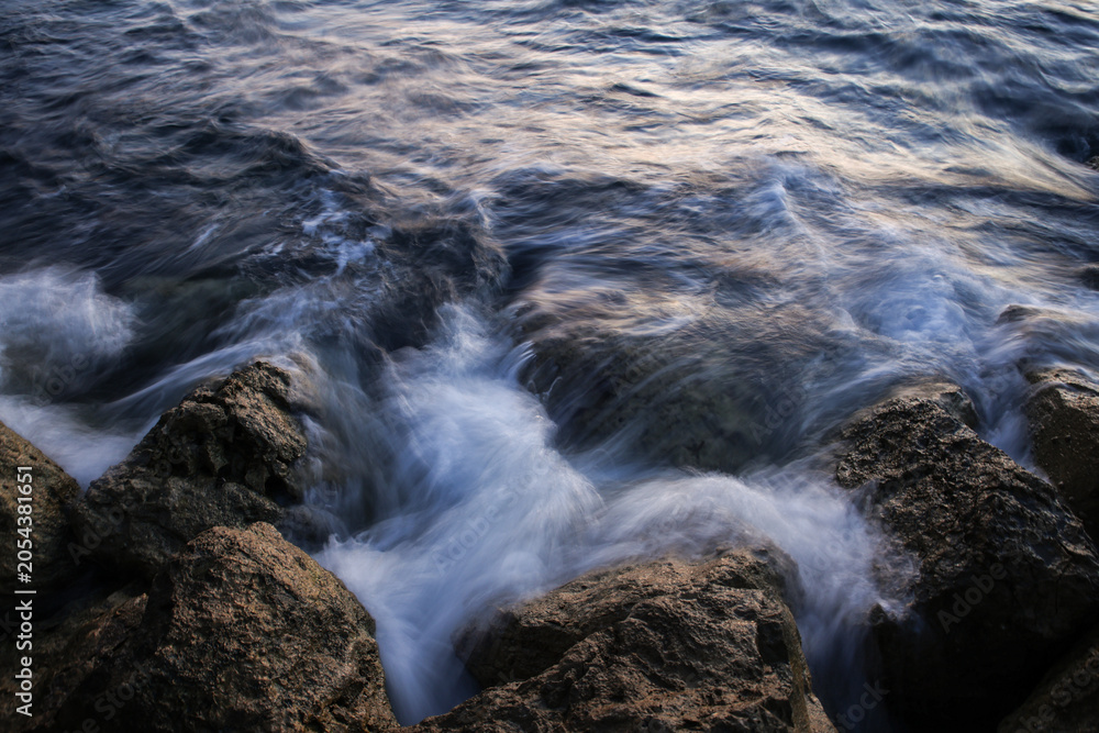 Fototapeta premium Artistic Long Exposure Photography of Rushing Ocean Waves Crashing Over Rugged Dark Coastal Rocks at Twilight