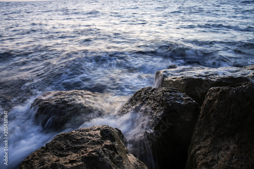 Artistic Long Exposure Photography of Rushing Ocean Waves Crashing Over Rugged Dark Coastal Rocks at Twilight