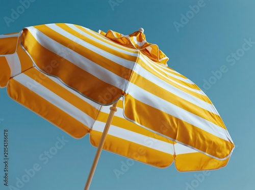 Bright yellow and white striped beach umbrella against a clear blue sky