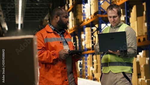 Schilderij op canvas Two employees checking parcel status on package tracking interface, working in industrial depot for import export operations