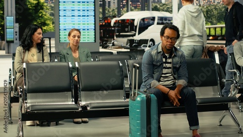 Tableau sur toile Black solo traveler waiting in busy coach station before intercity departure, sitting with baggage and backpack while reviewing schedule and departure time, long-haul highway bus travel