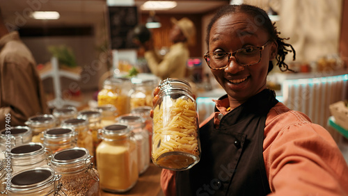 Fotografi POV merchant promoting her zero waste eco store business, recording video on social media to present homegrown produce and organic natural pantry supplies