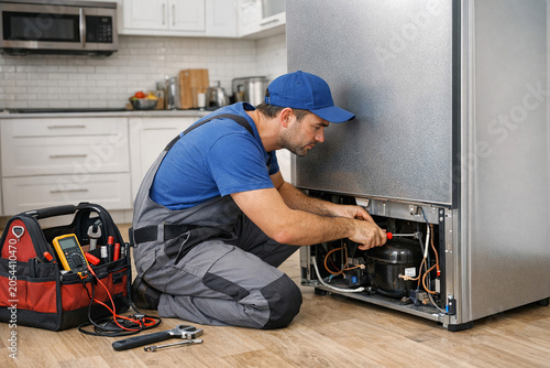 A man in blue working on the inside of a large silver fridge.