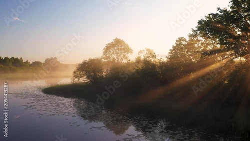 Golden sun rays illuminating morning fog and trees near water