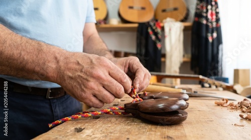 Instrument maker threading colorful strings into wooden castanets on a workbench