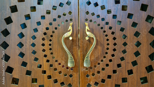 Canvas Print Pair of brass peacock door handle on carved wooden door with geometric cutout pa