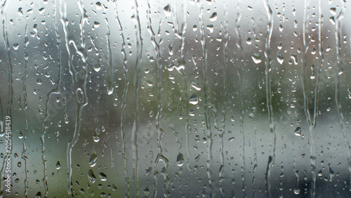 Rainwater droplet running down transparent glass window pane on rainy day with blur background