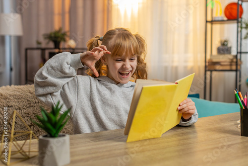 Bild auf Leinwand Young girl exploring dinosaur pictures in a book at home, reacting with excitement and imitating a roar
