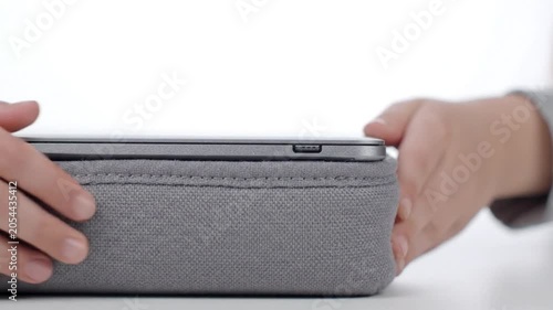 A person placing a smartphone into a gray fabric phone case on a white surface in this close-up video.