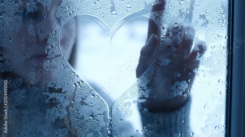 A person's hand touches a heart shaped mark on a foggy window in a video