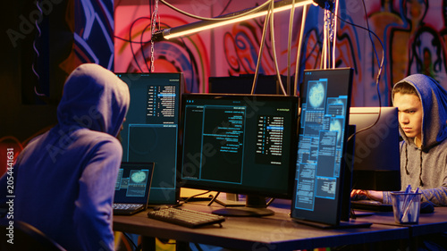 Fotografie Malicious computer specialists in secret abandoned warehouse working together to get past anti tamper measures implemented by companies to protect their software, uploading crack to torrent websites