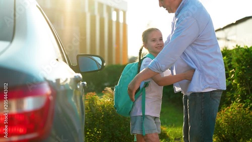 Happy papa hugs little girl getting ready lesson elementary school in schoolyard. Child education. Family happiness. Father walks daughter school with backpack, hugging on street next to car. Dad kid