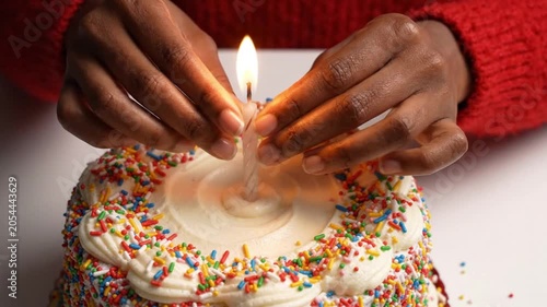 A person lighting a candle on a birthday cake with colorful sprinkles in a cozy video setting.