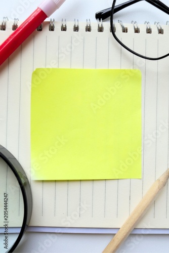 Top view of eyeglasses, magnifying glass, and red marker arranged around an open blank lined spiral notebook creating a frame with copy space, isolated on white background.