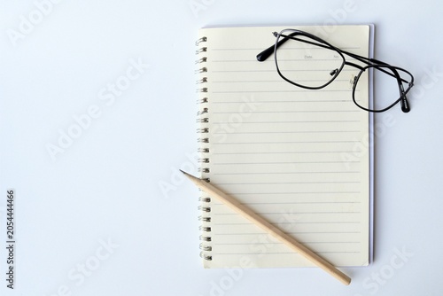 Top view of black frame eyeglasses and a wooden pencil on an open blank lined spiral notebook, isolated on white background, concept of education, studying, and workspace planning.