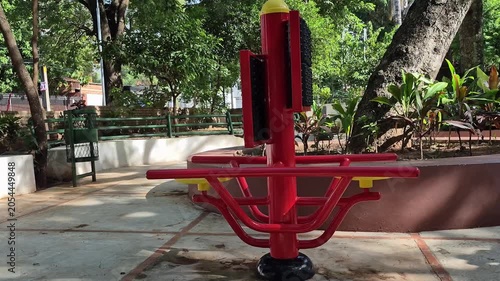 Red and yellow outdoor chest press rowing fitness station in tropical public park