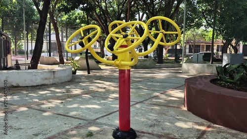 Wide pan of triple shoulder rotation fitness wheels in sunny public plaza, Latin America