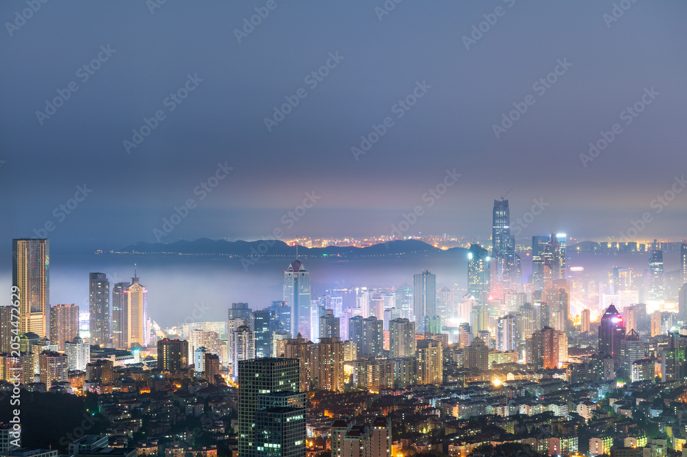 Fototapeta premium Qingdao Skyline at Dusk with Mist and Illuminated Skyscrapers, Shandong