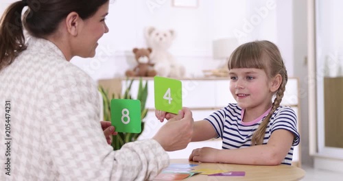 Speech therapist teaching girl numbers with colorful cards at wooden table indoors