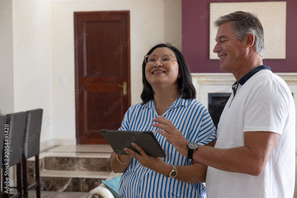 Obraz premium Diverse couple standing in living room, woman holding tablet, man gesturing toward screen