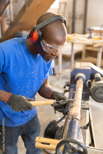 Wood lathe shaping cylindrical wooden blank on carpentry bench with wood shavings scattered