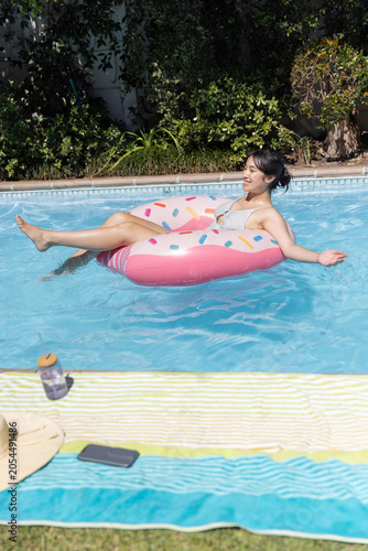 Pink donut pool float drifting on backyard pool water, displaying towel, hat, bottle, phone