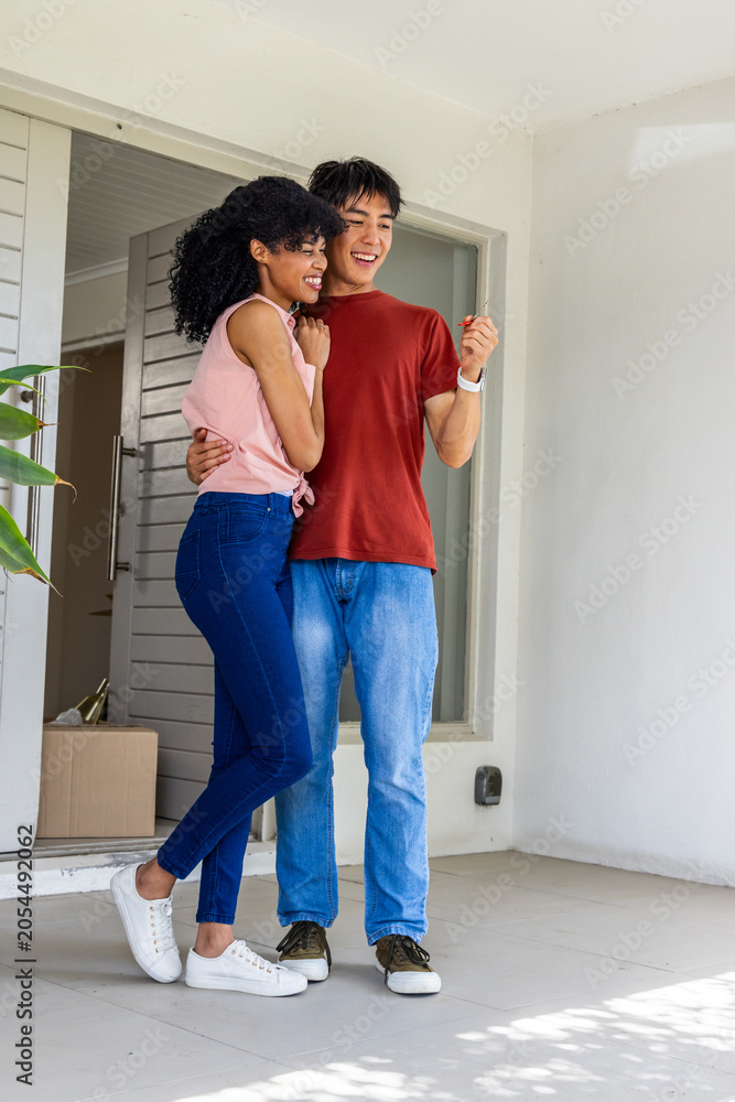 Obraz premium Couple hugging doorway man holding key causing motion real estate icons over box marking move-in