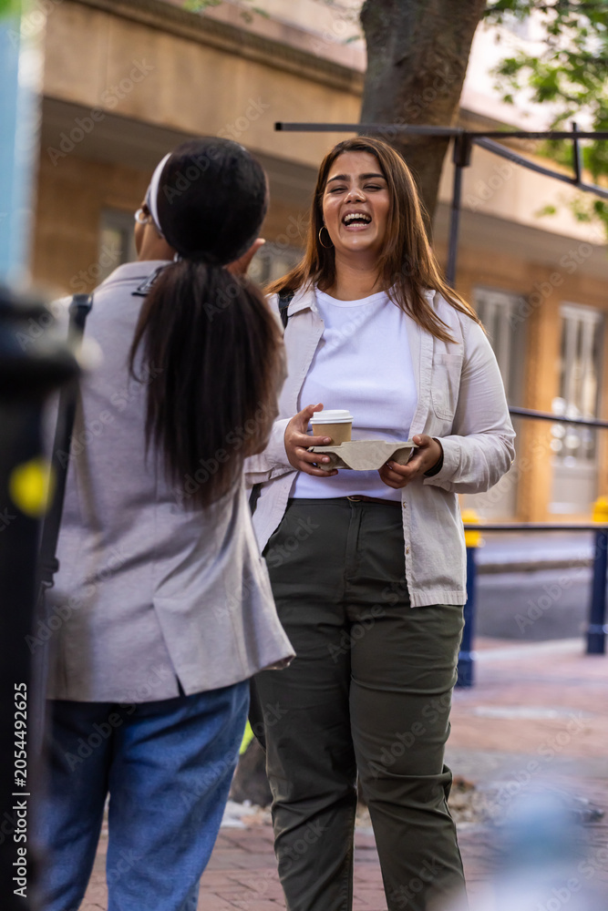 Fototapeta premium African American female friends laughing and chatting on sidewalk, one holding takeaway coffee tray