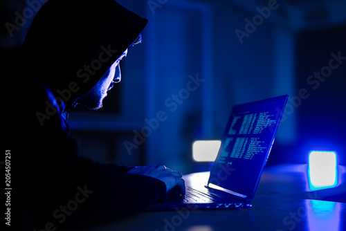 Принти на полотні Mysterious hacker in black hoodie stealing confidential data on laptop