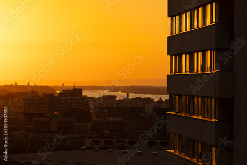 Fotografía Golden sunset over modern city skyline with river and residential buildings