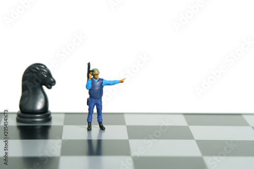 Miniature people toy figure photography. Protection strategy concept. A security officer standing above chessboard. Isolated on white background.