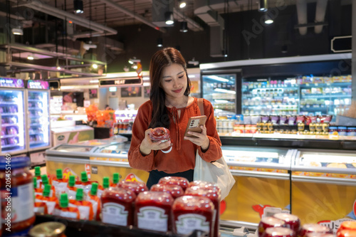 Obraz na plátne Woman comparing product labels and prices using smartphone