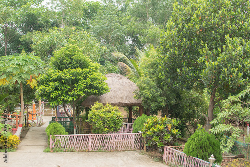 Bild auf Leinwand A peaceful garden retreat with a charming thatched hut, vibrant trees, and landscaped greenery all around
